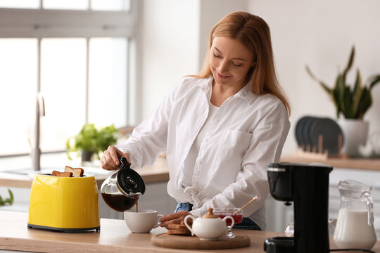 Mature woman making tasty toasts and drinking coffee in kitchen - Powered by Adobe