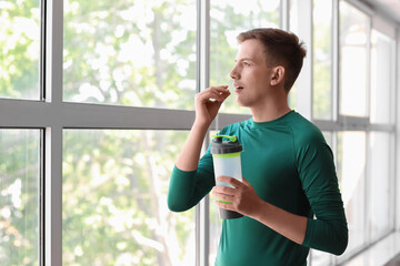 Young man with bottle of water taking vitamin supplement at home