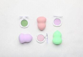 Different cosmetics and makeup sponges on light background