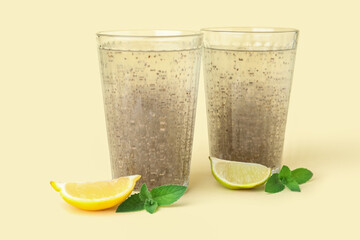 Glasses of drink with chia seeds, lemon and mint leaves on yellow background