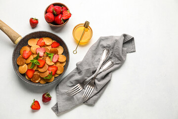 Frying pan with mini pancakes, strawberry and bowl with honey on white background