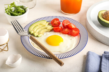 Plate with tasty fried egg, tomatoes and avocado on light table