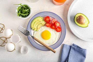 Plate with tasty fried egg, vegetables and greens on light background