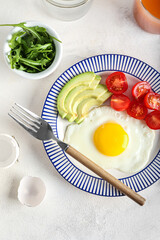 Plate with tasty fried egg, tomatoes and avocado on light background