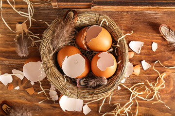 Nest with broken egg shells and feathers on wooden background