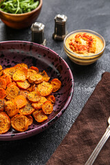 Bowl of tasty baked carrots on dark background, closeup