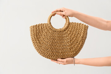 Woman holding rattan handbag on light background, closeup