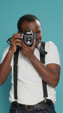Vertical video: Portrait of male photographer taking pictures with professional camera, using photography equipment to capture creative photos. Focused man shooting with digital lens for production.