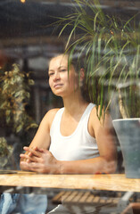 Fototapeta na wymiar a girl in a white t-shirt sits in a cafe, view through the glass