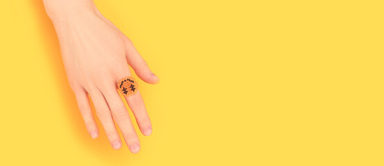 Banner with female hand with smiley ring made of beads on a yellow background. Place for text.