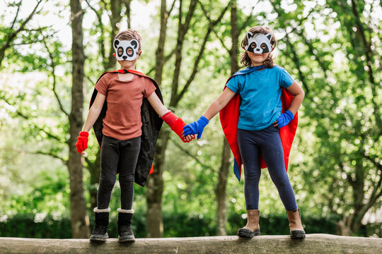 Siblings in superhero costumes standing on log