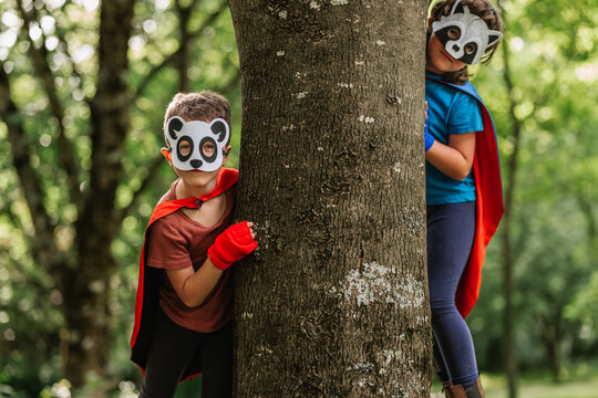 Little superheroes in animal masks hiding behind tree