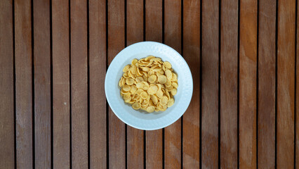 Corn flakes in a white plate in the middle on a wooden background for breakfast