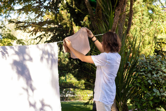 Young Unrecognizable Man From The Back Hanging Out The Washing In The Home Garden In Summer Time