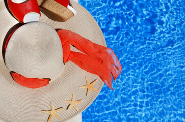 Women's hat, sandals and starfish next to the pool.