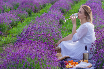 a girl holds a glass of white wine against the backdrop of a lavender field. A girl drinks wine in a lavender field.