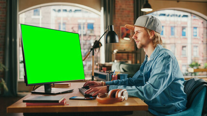 Young Handsome Man Working from Home on Desktop Computer with Green Screen Mock Up Display. Student...