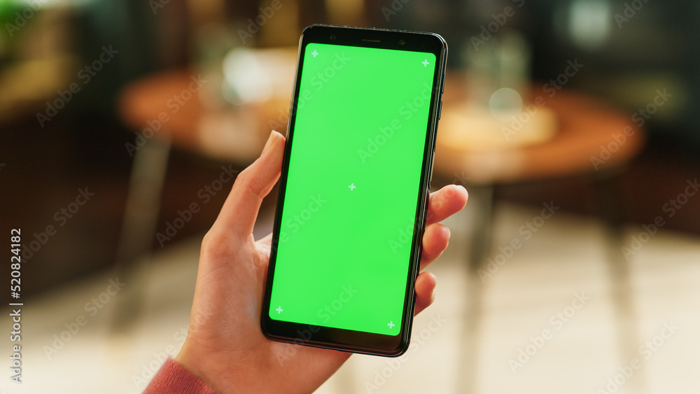 Poster feminine hand holding a smartphone with green screen mock up display. female in casual clothes resti