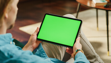Young Man Scrolling and Tapping on Content on Tablet Computer with Green Screen Mock Up Display....