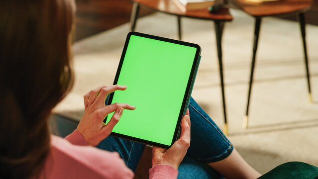 Female Scrolling and Tapping on Content on Tablet Computer with Green Screen Mock Up Display. Woman Relaxing at Home, Reading Social Media Posts on Mobile Device. Close Up Over the Shoulder Photo.