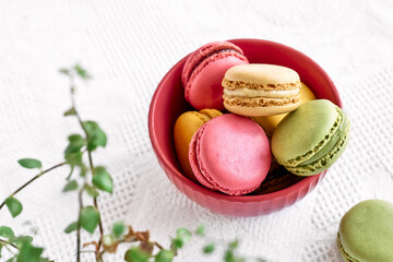 Colorful french macarons in pink bowl on white tablecloth. Tasty cakes macaroon of different colors. Strawberry, lime and lemon almond cookies, pastel colors.