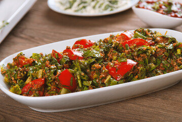 Tabbouleh salad with bulgur, tomatoes, parsley and green onion in plate on wooden table. Traditional middle eastern or arab dish.