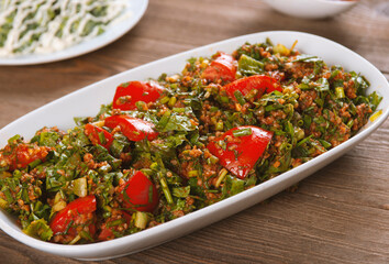 Tabbouleh salad with bulgur, tomatoes, parsley and green onion in plate on wooden table. Traditional middle eastern or arab dish.
