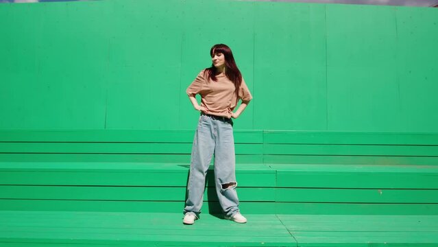 Young woman dancing hip hop on green background wall. Modern dance choreography. Female professional dancer showing dance movings. Musical video.