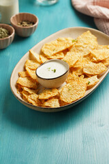 An oval plate with cheese tortilla chips and a yoghurt dip on a blue wooden surface