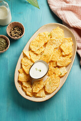 An oval plate with cheese tortilla chips and a yoghurt dip on a blue wooden surface