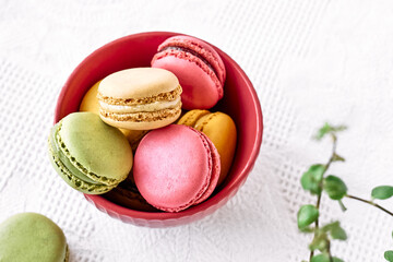 Colorful french macarons in pink bowl on white tablecloth. Tasty cakes macaroon of different colors. Strawberry, lime and lemon almond cookies, pastel colors.