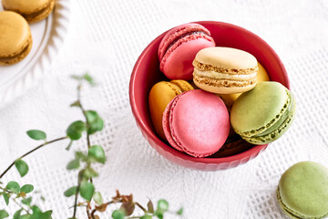 Colorful french macarons in pink bowl on white tablecloth. Tasty cakes macaroon of different colors. Strawberry, lime and lemon almond cookies, pastel colors.