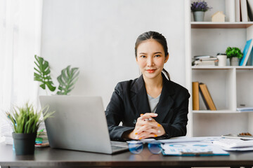 Young Pretty Asian businesswoman working in office, using laptop and looking to camera.