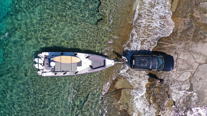 Aerial top view photo of speed boat on transport trailer being towed by truck from emerald sea shore to land