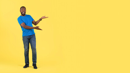 Fototapeta premium Excited Black Guy Gesturing Pointing At Free Space, Yellow Background