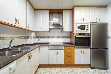 Old style empty kitchen with cabinets, tiled walls, marble countertop and typical household appliances