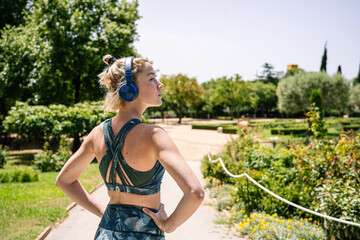 young blonde woman listens to music with headphones ready to start running in the park