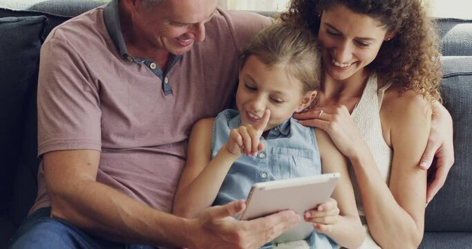 Family browsing online, streaming movies or watching videos on a tablet together on their living room sofa at home. Happy, carefree and curious girl scrolling on an educational app with parents