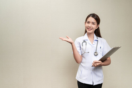 Asian Doctor Woman With Long Brown Hair A Happy Expression With Her Hand Pointing At Text Copy Space Isolated From Background Holding A Writing Board And Has A Heartbeat Stethoscope On The Neck