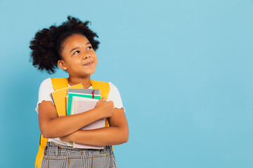 Happy African American schoolgirl holding books on blue background, back to school concept.