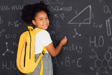 Happy African American schoolgirl solving problems near the blackboard at school, back to school concept.