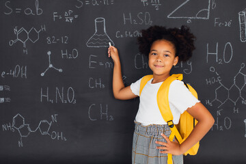 Happy African American schoolgirl solving problems near the blackboard at school, back to school...