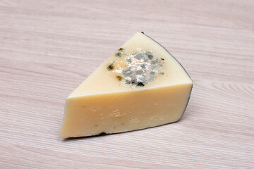 moldy piece of cheese on a wooden light surface