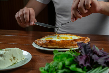 Man eating adjar Khachapuri. Georgian national pie khachapuri with egg and cheese in the white plate  on wooden background.