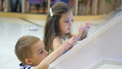 Close-up.A beautiful little girl with a younger brother using a touch terminal in a shopping mall.The child uses a touch terminal to search for the right store.The concept of people and technologies. 