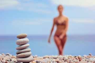 Stack of pebble stones at the beach with a beautiful woman behind.