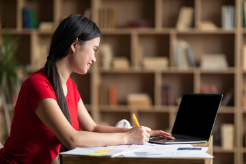 Happy young asian female student watching online lesson on laptop with empty screen in cabinet