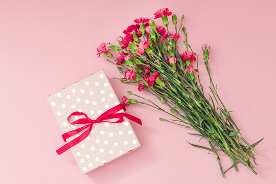Red mini carnation and gift box. Concept of giving present at mother's day as surprise, flat lay, top view On pink Background