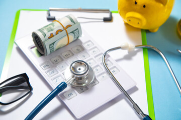 Piggy bank with stethoscope, money and calculator on the blue background.