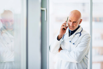 Male doctor using mobile phone while standing on the hospital's foyer